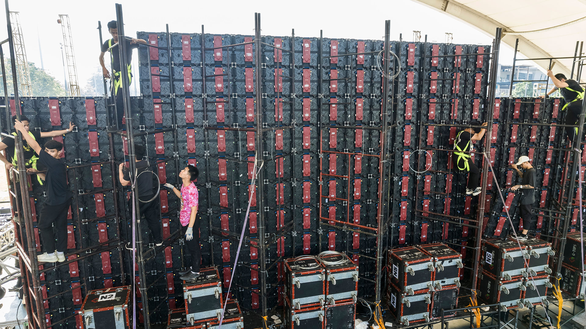 A team of workers collaborates on constructing a large wall, ensuring stability for outdoor event displays.