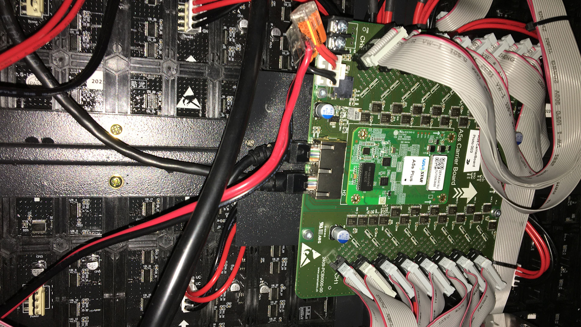 A computer board with wires, featuring Parasigna’s EMC Filter Cards behind a large LED display.